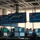 Stock market monitors showing rising charts during a rally led by chip and travel stocks.