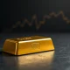 Gold bullion bar with US dollar chart in background, representing gold price recovery amid dollar weakness per OCBC analysis.
