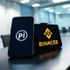 Smartphone showing Pi Network app and Binance logo on a desk, representing a potential crypto exchange listing.