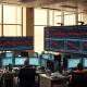 Stock market trading floor with monitors showing declining technology sector charts.