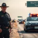 A police officer interacts with a Waymo self-driving car on a highway shoulder.