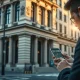 A person analyzes financial data on a smartphone outside a bank building, representing investment research.