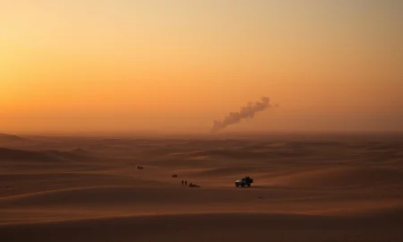 A desert landscape with a distant smoke plume, representing ongoing conflict in the Middle East.