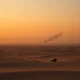 A desert landscape with a distant smoke plume, representing ongoing conflict in the Middle East.