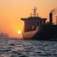 Cargo ship in Strait of Hormuz at sunrise, representing geopolitical risk for USD/SGD