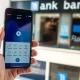 Smartphone showing a fintech banking app next to a traditional UK bank branch.