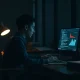 A person studying AI concepts on a laptop in a dimly lit tech office, surrounded by books and notes.
