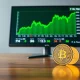 Computer monitor displaying green altcoin trading charts with a Binance coin on a desk in a professional office setting.