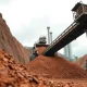 Large-scale bauxite mining operation with machinery and conveyor belt under overcast sky
