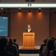 Cat Wu speaking at Code with Claude conference in San Francisco, with AI interface on screen behind her.