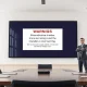 Anthropic executive standing in front of a digital warning about unauthorized share trading in a modern boardroom