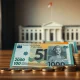 Australian dollar banknotes and coins on a desk with Parliament House in the background, representing budget and economic policy.
