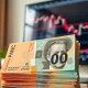 Close-up of Australian dollar banknotes with a blurred forex chart in the background