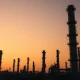 Oil refinery distillation towers at dusk, representing Brent crude supply uncertainty after Iran conflict.