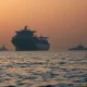 Oil tanker anchored near the Strait of Hormuz at dawn with naval presence