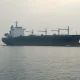 Oil tanker navigating the Strait of Hormuz under overcast skies with naval presence.