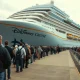 Passengers waiting on the pier near a docked Disney cruise ship after boarding was canceled.