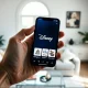 Person holding a smartphone showing a unified Disney app interface with streaming, parks, and cruise options.
