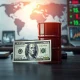 US dollar banknote and crude oil barrel on a desk with financial charts in background