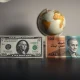 US dollar and Iranian rial banknotes on a desk with a globe in the background.