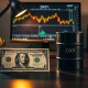 US dollar and crude oil barrel on desk with financial charts on monitor
