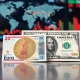 Euro and US dollar banknotes on a desk with a financial news screen in the background