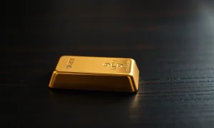 Gold bar on dark wooden surface with soft lighting, representing flat gold prices near $4,700.