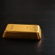 Gold bar on dark wooden surface with soft lighting, representing flat gold prices near $4,700.