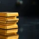 Gold bars and coins on a dark reflective surface representing safe-haven demand amid market uncertainty.