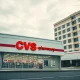 Exterior of a CVS pharmacy with a hospital building in the background under overcast sky