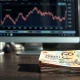Stack of Indonesian rupiah banknotes on a desk with a financial chart monitor in the background