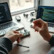 Hands assembling a hardware prototype kit with an AI chatbot interface on a laptop in a modern workshop