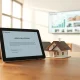 Digital tablet showing a home loan approval app next to a small model house on a desk in a modern office.