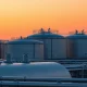 Natural gas storage facility at sunset with warm sky indicating hot weather
