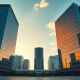Two modern financial towers representing Pimco and Apollo stand opposite each other at golden hour in a city plaza.