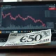 British Pound Sterling banknote on desk with laptop showing declining GBP/USD chart and London skyline in background