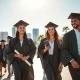 Recent college graduates in caps and gowns walking in a sunny Southern city plaza with a modern skyline in the background