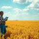 Farmer checking soybean prices on tablet in a field under cloudy sky