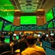 Stock exchange trading floor with green screens showing rising market indices and stock tickers