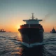 A cargo ship sailing through the Strait of Hormuz, with oil tankers visible in the distance.