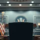 Empty podium in a U.S. government briefing room with American flag, symbolizing diplomatic tension