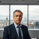 UBS CEO Sergio Ermotti in a boardroom with a serious expression, European city skyline in background