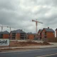 Stalled UK housing construction site with idle cranes and a weathered SOLD sign under grey sky