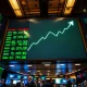 A view of a stock market board showing green numbers and an upward trend on a busy trading floor.