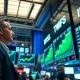 Traders on a stock exchange floor watching green screens showing record high S&P 500 index levels.