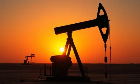 Oil pumpjack silhouette against sunset sky with faint US and Iran flags