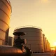 Oil storage tanks at a terminal under a sunset sky, representing crude oil supply and market conditions.