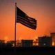 WTI crude oil storage tanks with American flag at sunset, representing geopolitical oil supply risk.