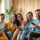 Group of young adults laughing together while using smartphones in a sunlit modern living room
