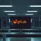 Empty office desks with code on monitors representing GitLab layoffs and restructuring